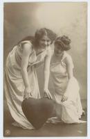 [Two women posed together in simple white gowns with heart prop] 779/1