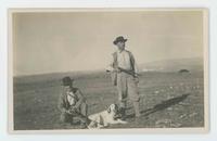 [2 men hunting (both are carrying shotguns) with a dog]