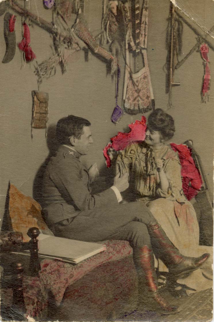 [Man and woman sitting on a daybed with Native American objects hanging on the wall behind them]