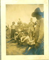 [Group of cowboys at leisure standing & sitting by barbed wire fence with chuckwagon in background]