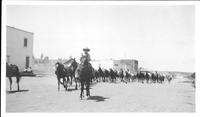 [Cowgirl on horse leading herd of horses through town]