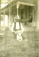 [Man sitting on dog resting watermelon on dog's back with house and porch behind]