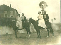 [Two pairs of well-dressed men and women; each couple sharing the back of a horse in front of house]