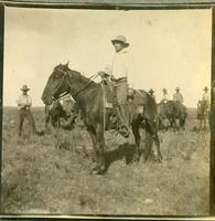 [Portrait shot of Cowboy in profile on horse with cowboys on horses in background]