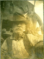 [Elderly mustachioed cowboy in medium shot in front of wagon wheel]