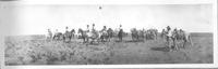 [Cowboys in various posed positions mostly on horseback with chuckwagon & horse herd in background]