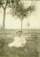 [Baby with hat sitting up in backyard]