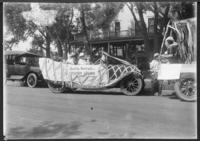 [Automobiles decorated for a parade sitting in front of a house]