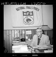 John Van Cronkhite sitting at desk, NFR sign in background